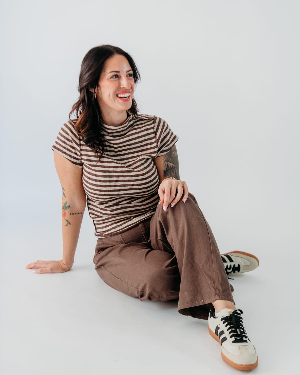 Jamee Fink, owner and photographer at Nice Boudie Studio, laughing on the studio floor in a striped tee