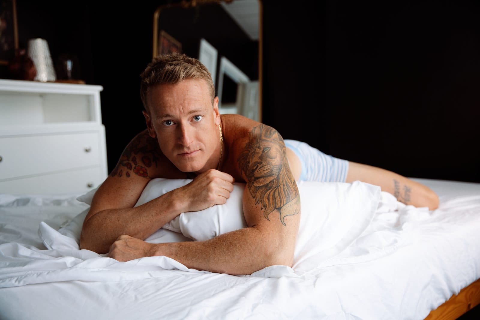 A smiling man lies on a white bed
