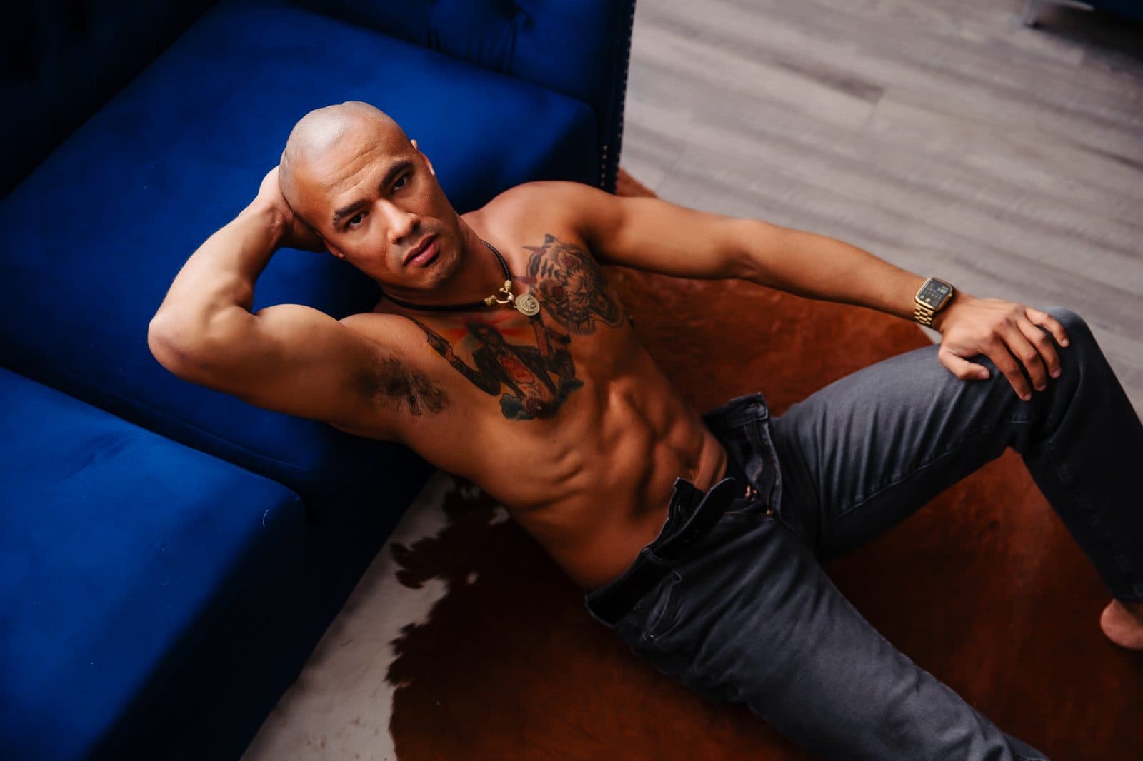 A shirtless man in jeans lies back on a cowhide rug by the navy couch