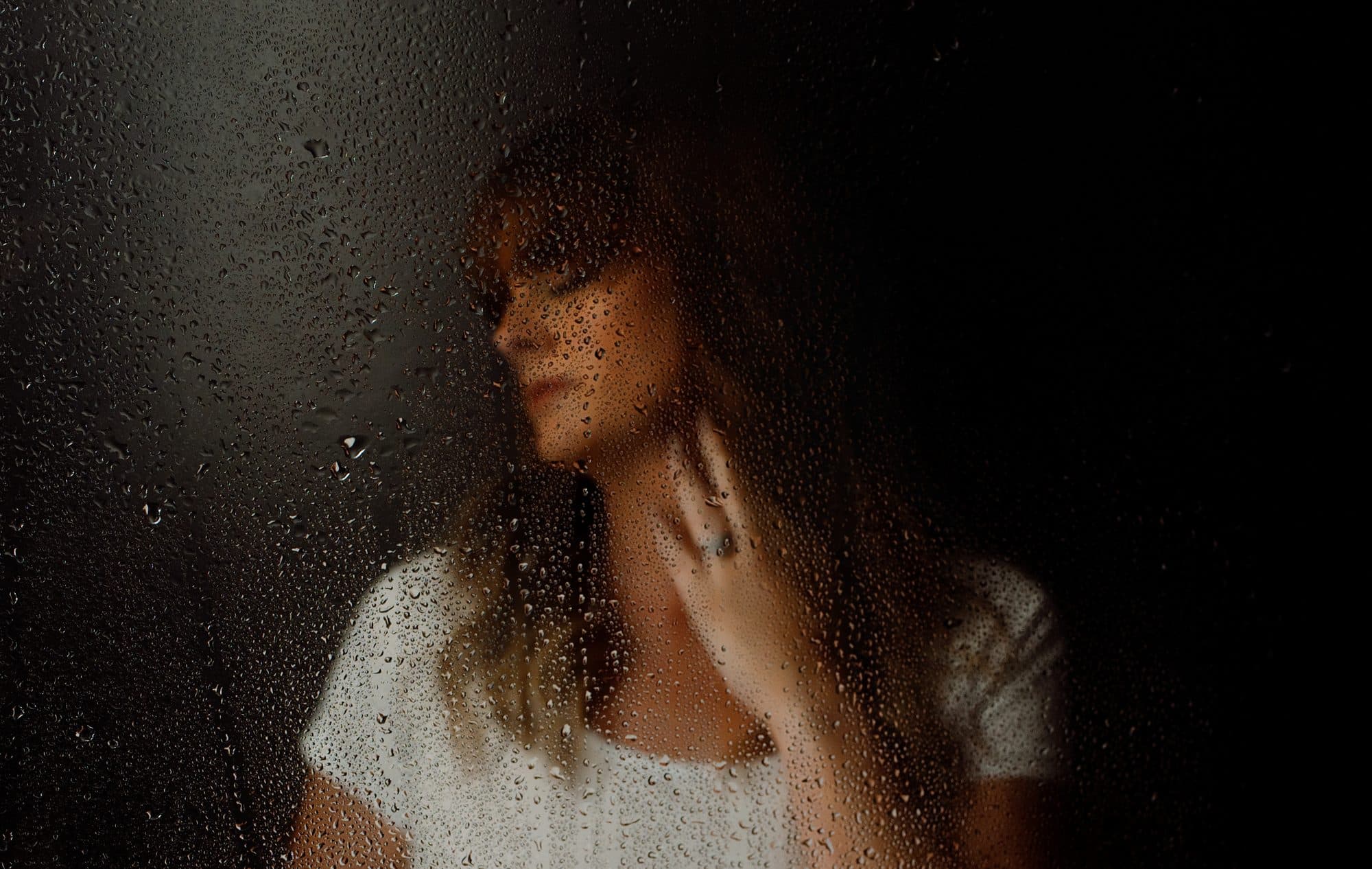 A client in a white crop top behind steamy shower glass dotted with water