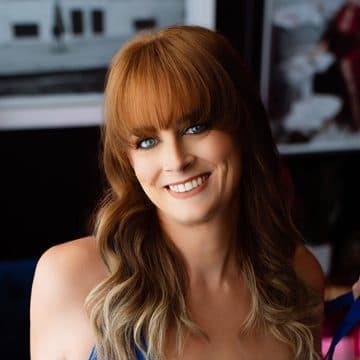 A smiling client with red hair in blue strappy lingerie on the navy velvet couch