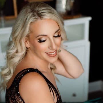A smiling blonde client in a black lace bodysuit sitting on teal satin sheets