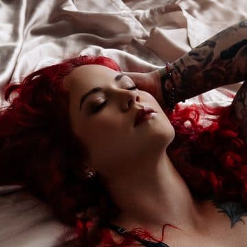 A client with red hair in black lingerie lying back at the foot of the bed in window light