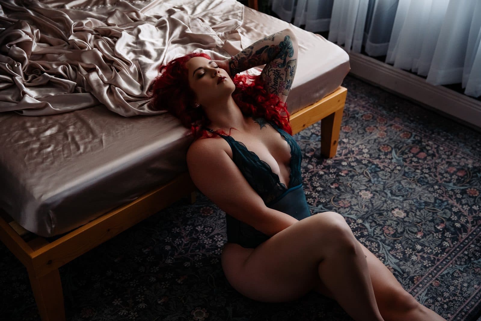 A client with red hair in black lingerie lying back at the foot of the bed in window light